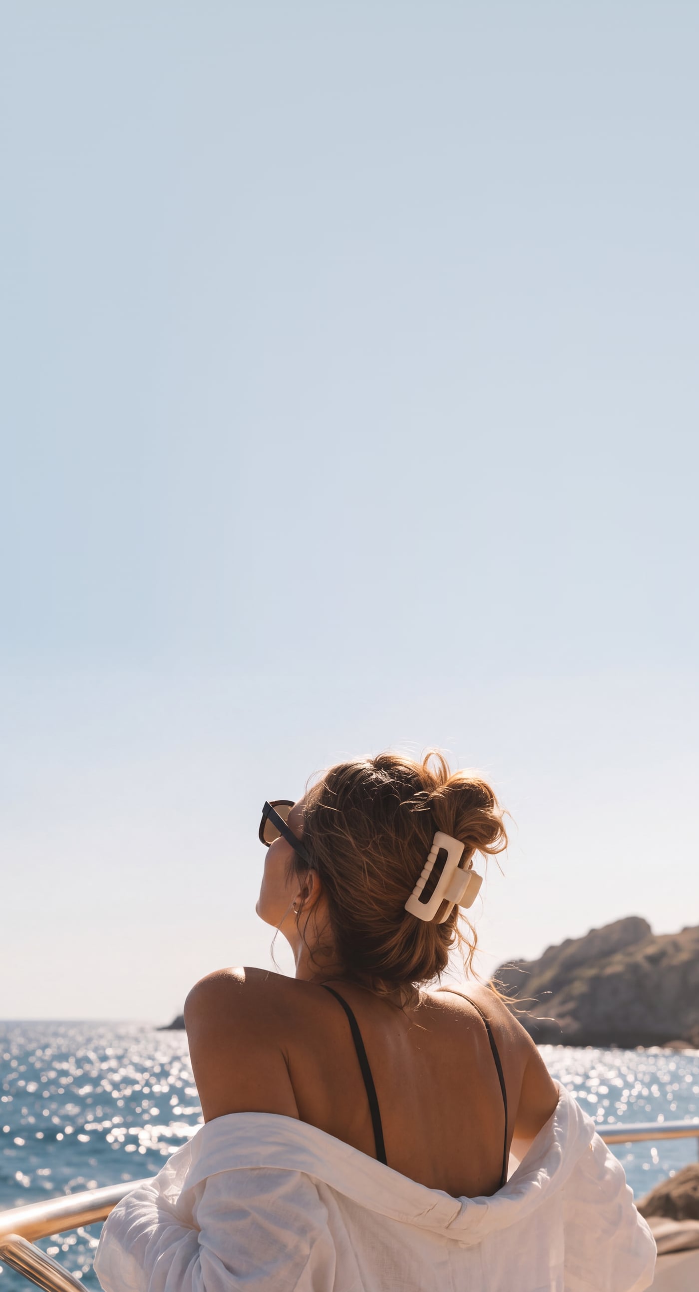 A woman on the deck of a boat, face turned to the sun, looking out over the sea